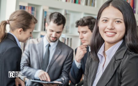 Three business people looking at a tablet with one businesswoman in the foreground smiling