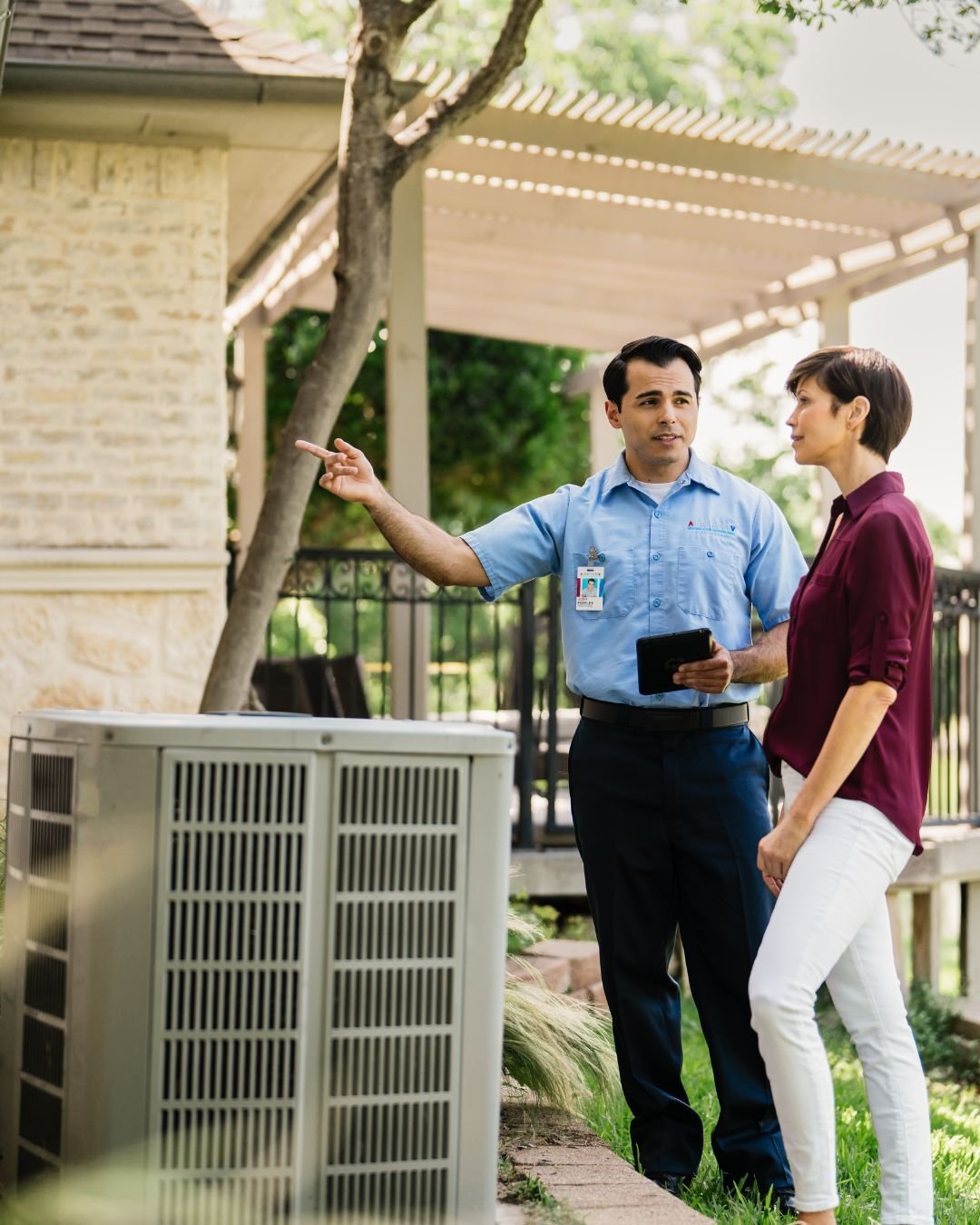 Professional HVAC technician inspecting an outdoor AC system and discussing service options with a customer, illustrating the value and revenue potential of an Aire Serv franchise.