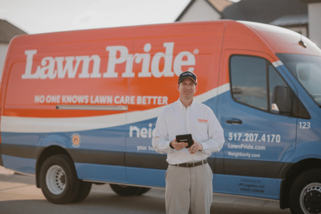 Lawn Pride, a Neighborly brand, service technician standing in front of a branded Lawn Pride lawn care van in a residential neighborhood, showcasing professional home lawn care services.